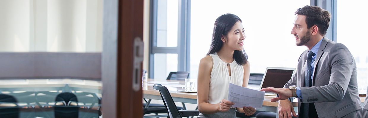 A woman is holding some documents and discussing with a man in suit at a meeting room. Image used for HSBC Branch Banking page.